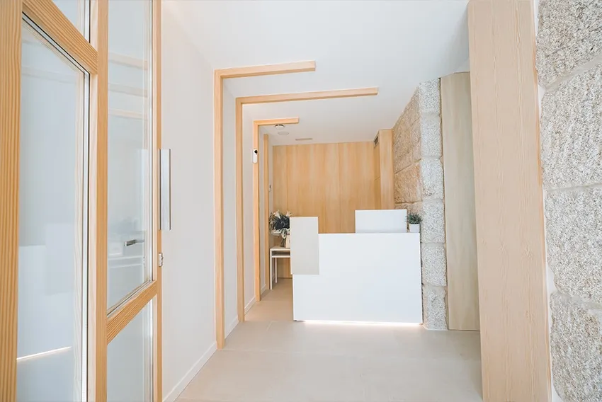 Recepción de la Clínica Dentalcom en Coruxo, con pared de piedra y acabados en madera clara
