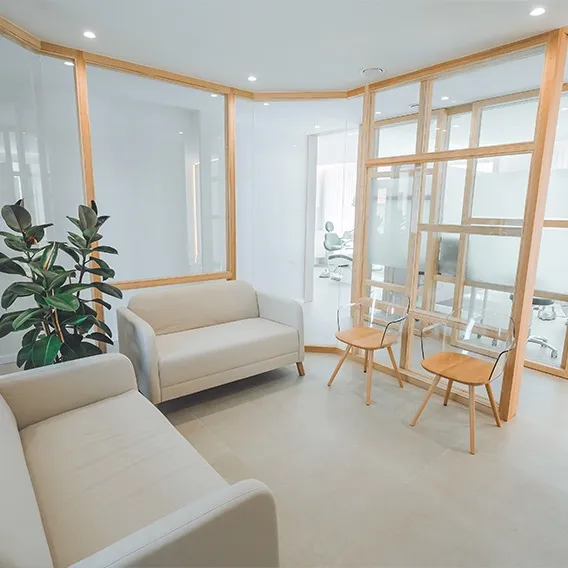 Sala de espera amplia y luminosa de la Clínica Dentalcom, con sofás y separaciones de madera